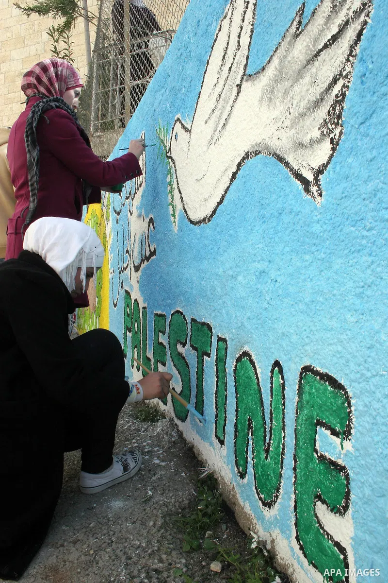 Palestinian students paint on the school wall as a former French football player Lilian Thuram (unseen) looks on during a visit to the divided city of Hebron, in the Israeli-occupied West Bank, on April 13, 2011. Thuram...
