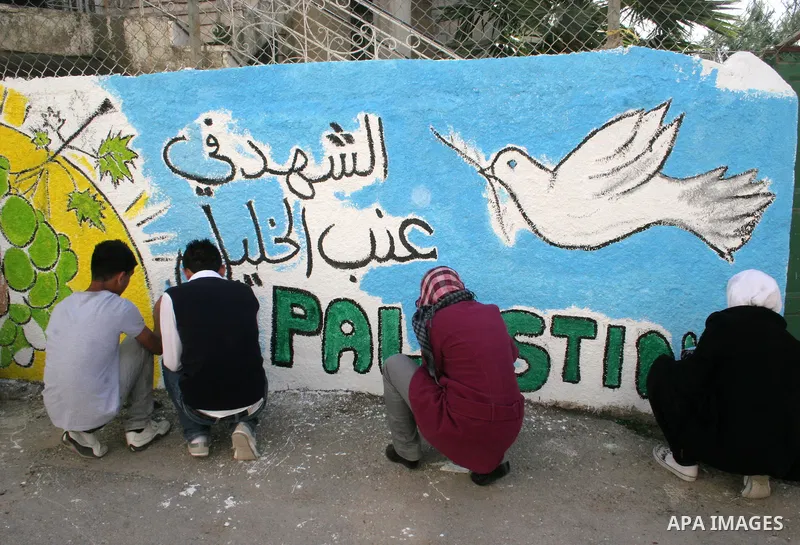 Palestinian students paint on the school wall as a former French football player Lilian Thuram (unseen) looks on during a visit to the divided city of Hebron, in the Israeli-occupied West Bank, on April 13, 2011. Thuram...