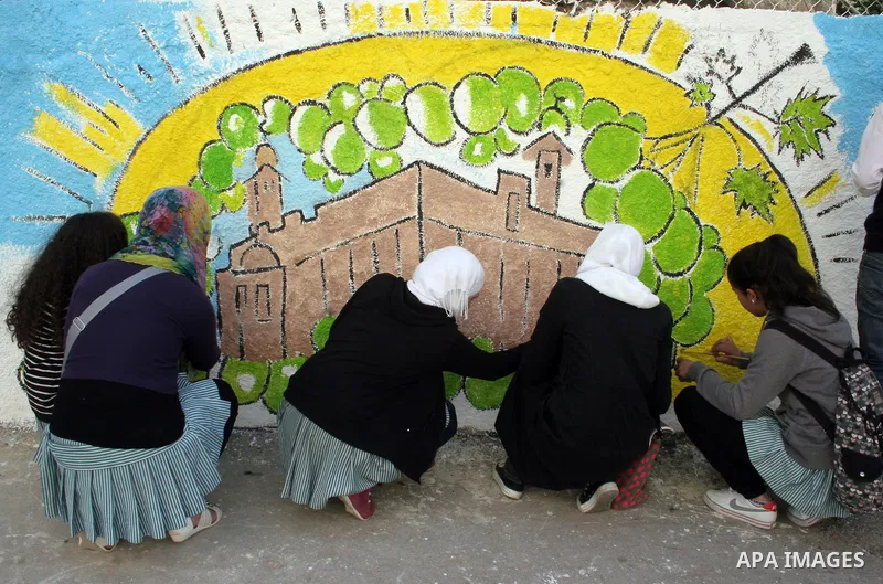 Palestinian students paint on the school wall as a former French football player Lilian Thuram (unseen) looks on during a visit to the divided city of Hebron, in the Israeli-occupied West Bank, on April 13, 2011. Thuram...