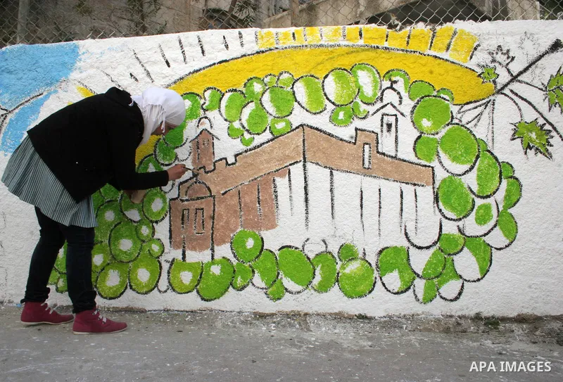 Palestinian students paint on the school wall as a former French football player Lilian Thuram (unseen) looks on during a visit to the divided city of Hebron, in the Israeli-occupied West Bank, on April 13, 2011. Thuram...