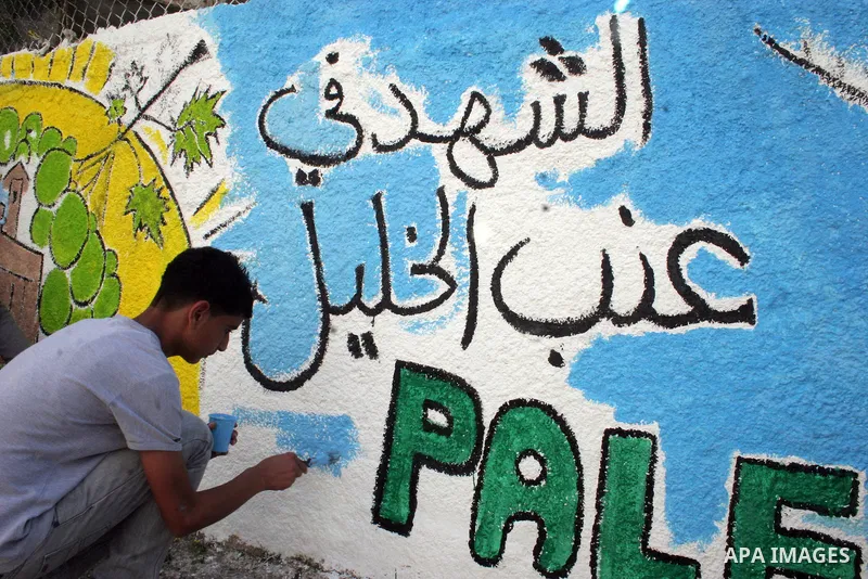 Palestinian students paint on the school wall as a former French football player Lilian Thuram (unseen) looks on during a visit to the divided city of Hebron, in the Israeli-occupied West Bank, on April 13, 2011. Thuram...
