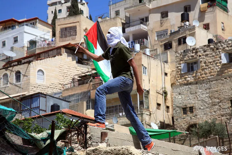 A masked Palestinian youth standing on top of a demolished building waves his national flag near Israeli riot policemen (unseen) in the east Jerusalem neighborhood of Silwan on April 15, 2011 following brief clashes betw...