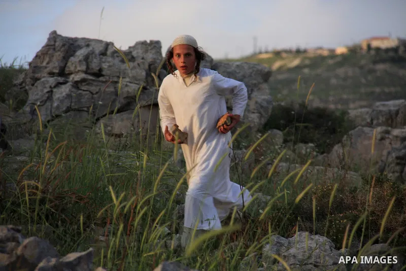 A Jewish settler boy throws rocks at Palestinian protesters, not seen, during clashes over farming land between the Jewish settlement of Bracha and the nearby West Bank village of Burin, near Nablus, Tuesday, April 19, 2...