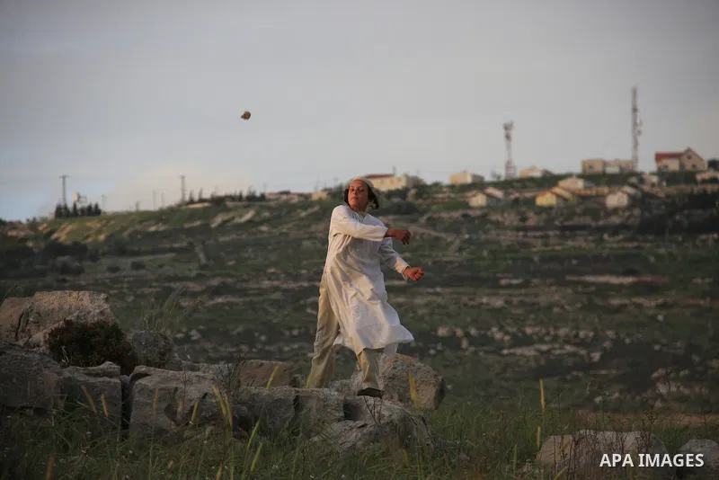 A Jewish settler boy throws rocks at Palestinian protesters, not seen, during clashes over farming land between the Jewish settlement of Bracha and the nearby West Bank village of Burin, near Nablus, Tuesday, April 19, 2...