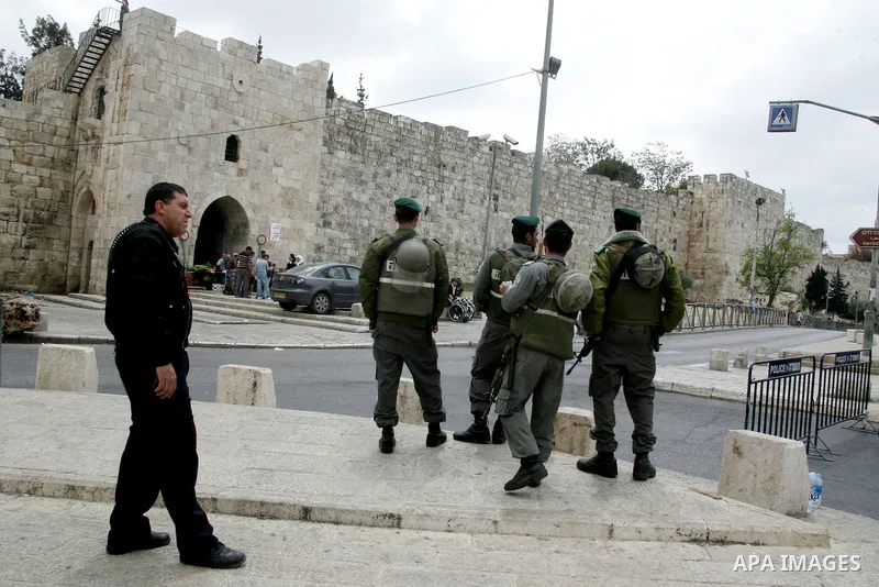 Palestinians walk past an Israeli police officers as they stand guards in the market of the old city of Jerusalem on April 21,2011 photo by MAhfouz Abu Turk