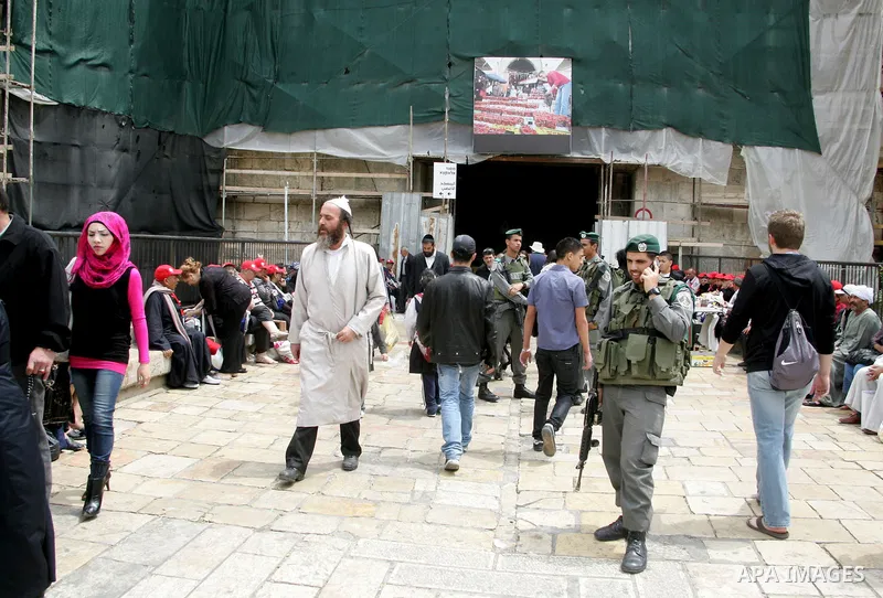 Palestinians walk past an Israeli police officers as they stand guards in the market of the old city of Jerusalem on April 21,2011 photo by MAhfouz Abu Turk