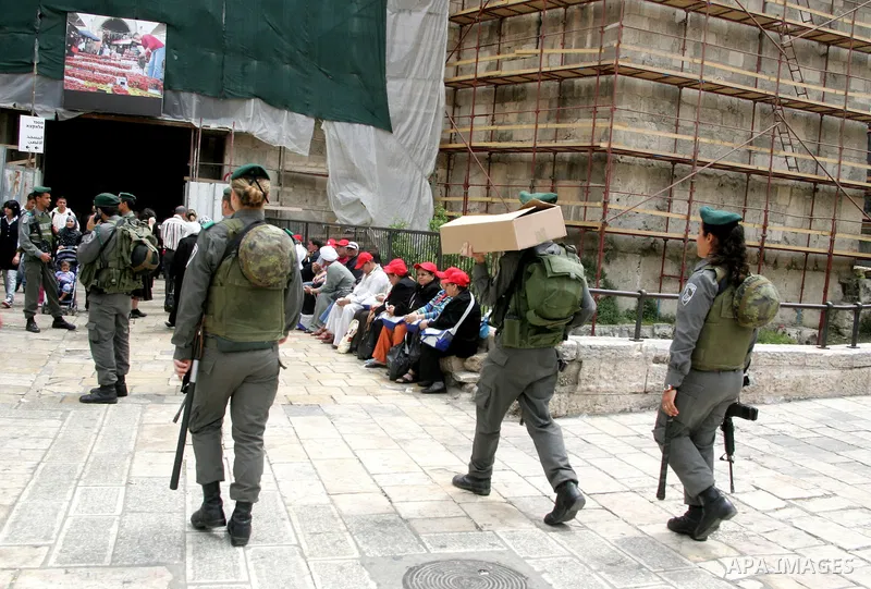 Palestinians walk past an Israeli police officers as they stand guards in the market of the old city of Jerusalem on April 21,2011 photo by MAhfouz Abu Turk