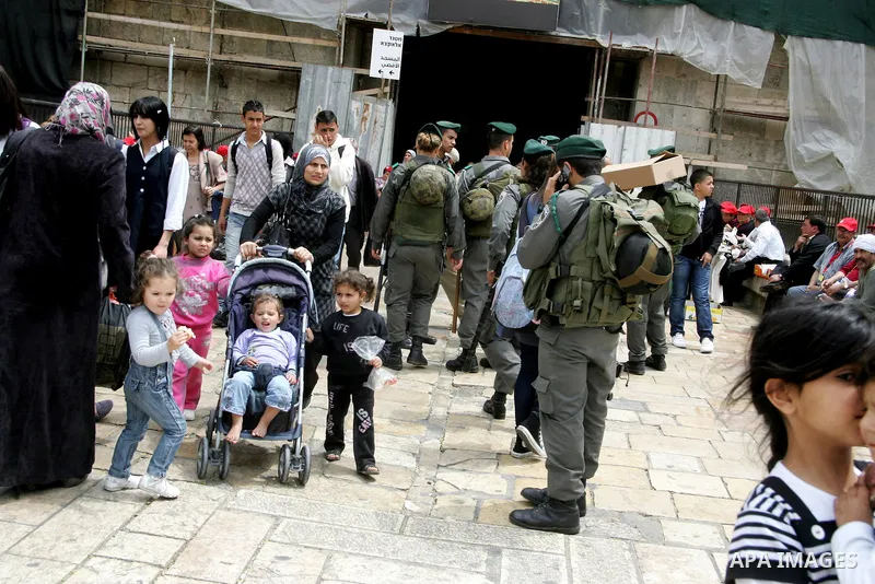Palestinians walk past an Israeli police officers as they stand guards in the market of the old city of Jerusalem on April 21,2011 photo by MAhfouz Abu Turk