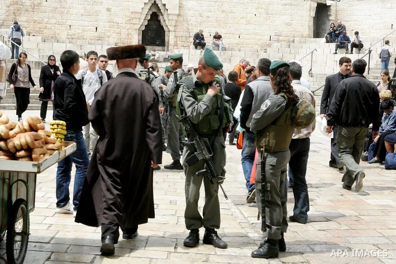 Palestinians walk past an Israeli police officers as they stand guards in the market of the old city of Jerusalem on April 21,2011 photo by MAhfouz Abu Turk