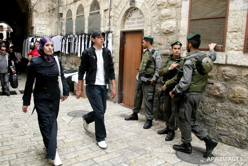 Palestinians walk past an Israeli police officers as they stand guards in the market of the old city of Jerusalem on April 21,2011 photo by MAhfouz Abu Turk