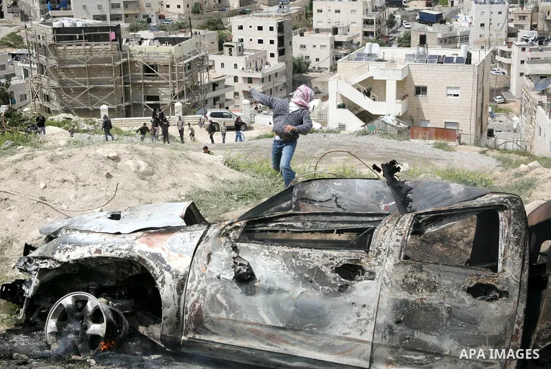 Masked Palestinian youths hurl stones toward Israeli soldiers near a burnt Israeli army vehicle on April 22, 2011 after it flipped over and was set alight by Palestinian youths in the flashpoint neighbourhood of Issawiya...