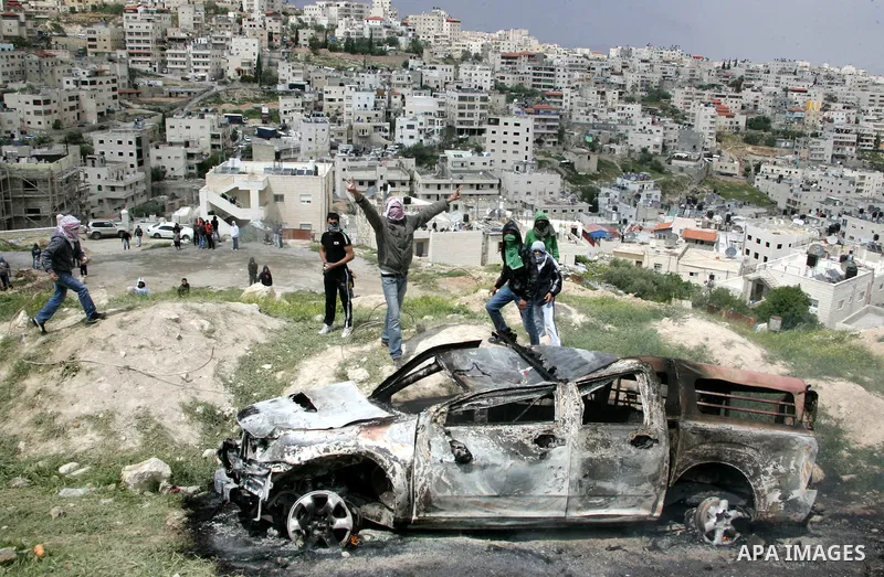 Masked Palestinian youths celebrate near a burnt Israeli army vehicle on April 22, 2011 after it flipped over and was set alight by Palestinian youths in the flashpoint neighbourhood of Issawiya in annexed east Jerusalem...