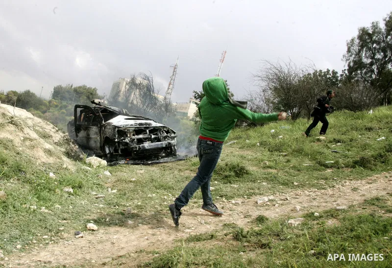Masked Palestinian youths hurl stones toward Israeli soldiers near a burnt Israeli army vehicle on April 22, 2011 after it flipped over and was set alight by Palestinian youths in the flashpoint neighbourhood of Issawiya...