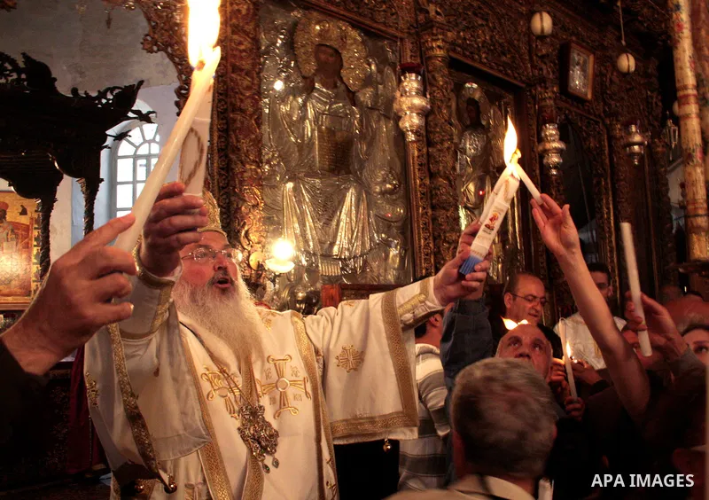 The head of the Greek Orthodox church in Bethlehem Bishop Theofilactos passes the 'Holy Fire' to worshippers brought from the Church of the Holy Sepulchre in Jerusalem during the 'Holy Fire' ceremony on the eve of the Or...