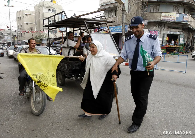 A Palestinian woman waves the Fatah party flag as she is helped to cross the street by a Hamas security man during celebrations to mark the political reconciliation agreement during a rally in Rafah, southern Gaza Strip,...