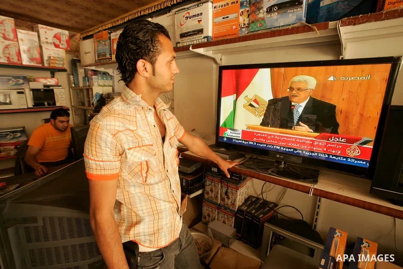 Palestinian youths watch on TV the signing of the political reconciliation agreement between Fatah and Hamas at a shop in the southern Gaza Strip town of Rafah on May 04, 201, as Palestinians in the West Bank and Gaza St...