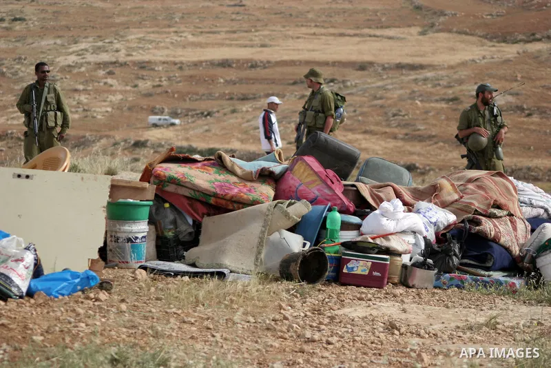 Israeli soldiers stand guard as members of a Palestinian family retrieve items from the rubble of their home after their shacks and tents were destroyed by Israeli bulldozers near the Jewish settlement of Sosia, in the v...