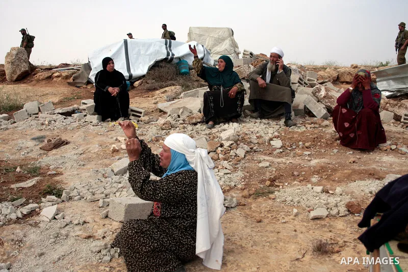 Israeli soldiers stand guard as members of a Palestinian family retrieve items from the rubble of their home after their shacks and tents were destroyed by Israeli bulldozers near the Jewish settlement of Sosia, in the v...