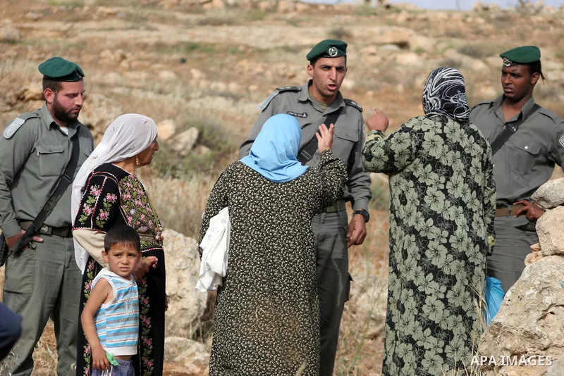 Israeli soldiers stand guard as members of a Palestinian family retrieve items from the rubble of their home after their shacks and tents were destroyed by Israeli bulldozers near the Jewish settlement of Sosia, in the v...
