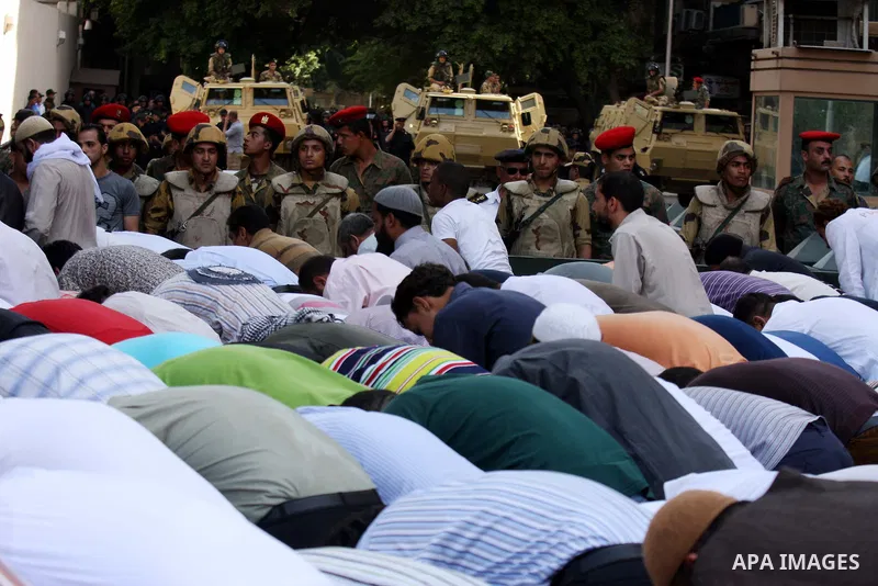 Egyptian military police stand guard as a boy holding the national flag stands before men performing their afternoon prayers during a protest outside the U.S. embassy in Cairo, Egypt, Friday, May 6, 2011, to denounce the...