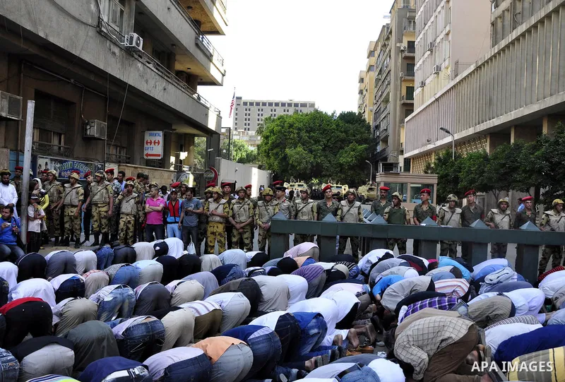 Egyptian military police stand guard as a boy holding the national flag stands before men performing their afternoon prayers during a protest outside the U.S. embassy in Cairo, Egypt, Friday, May 6, 2011, to denounce the...