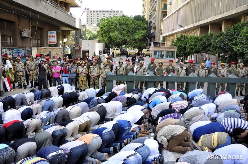 Egyptian military police stand guard as a boy holding the national flag stands before men performing their afternoon prayers during a protest outside the U.S. embassy in Cairo, Egypt, Friday, May 6, 2011, to denounce the...