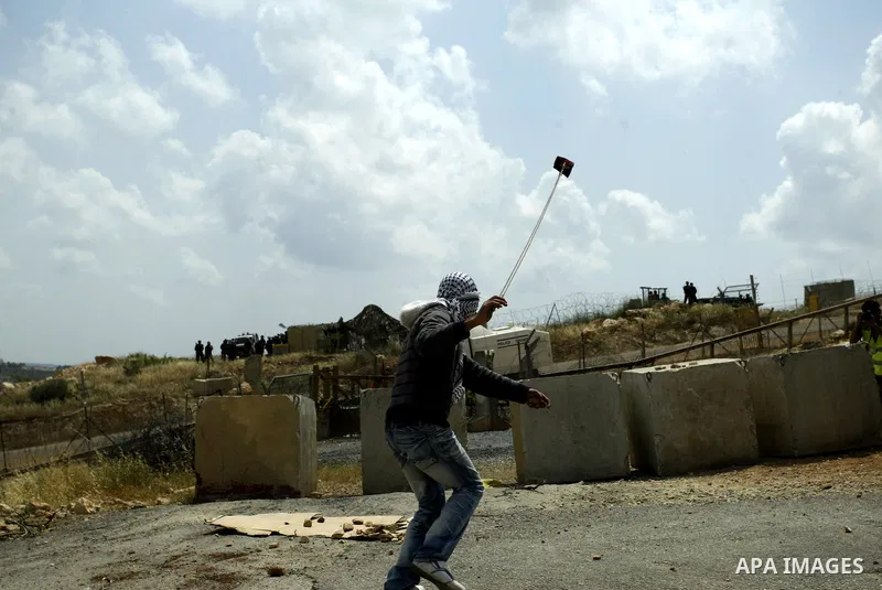 A masked Palestinian demonstrator uses a sling-shot to hurl stones at Israeli troops during a protest against Israel's controversial separation barrier and to mark the 63th anniversary of "Nakba" (catastrophe) on May 13,...