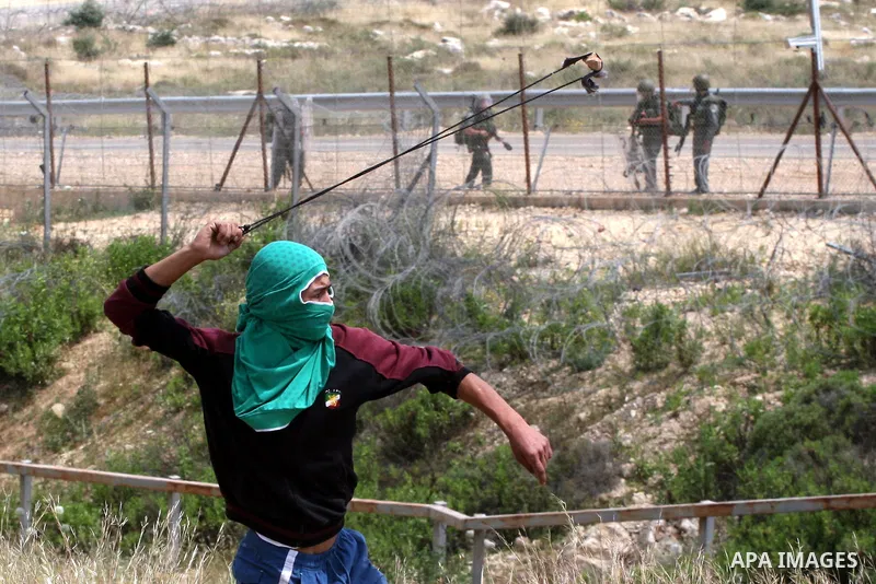 A masked Palestinian demonstrator uses a sling-shot to hurl stones at Israeli troops during a protest against Israel's controversial separation barrier and to mark the 63th anniversary of "Nakba" (catastrophe) on May 13,...