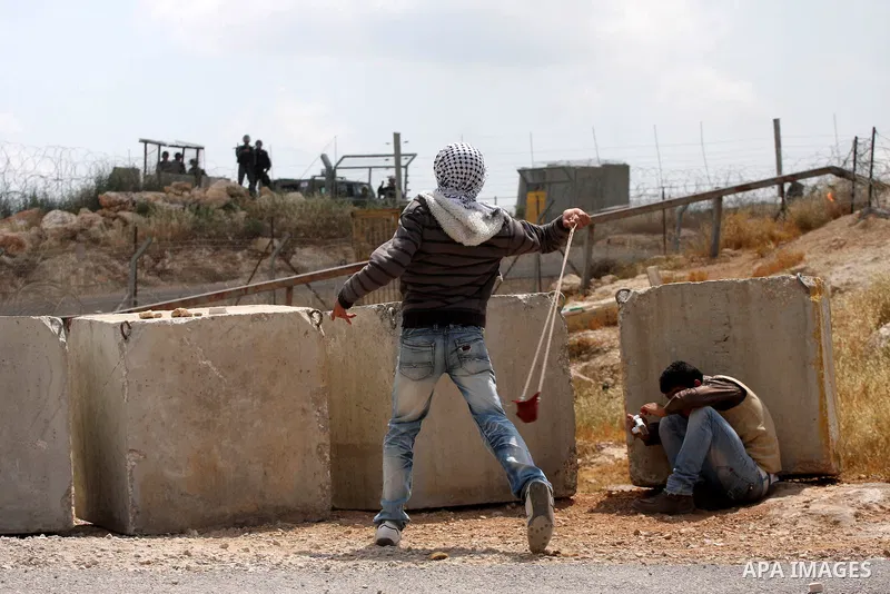 A masked Palestinian demonstrator uses a sling-shot to hurl stones at Israeli troops during a protest against Israel's controversial separation barrier and to mark the 63th anniversary of "Nakba" (catastrophe) on May 13,...