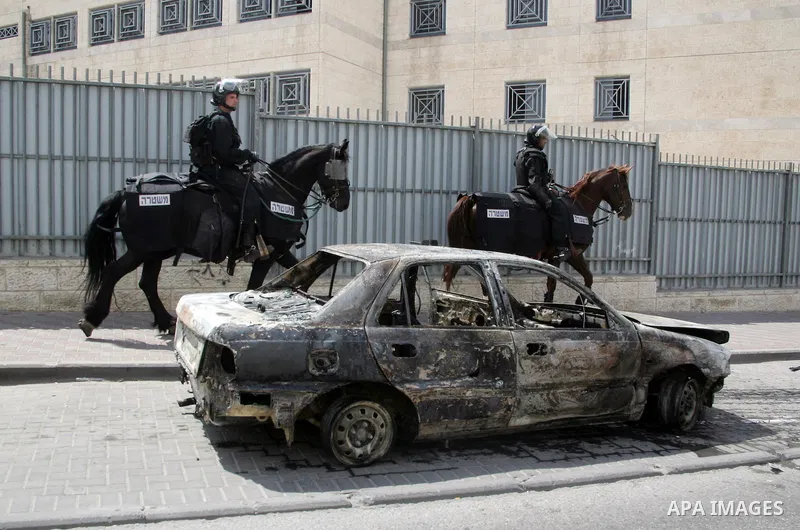An Israeli border policeman rides past a car which was torched during riots in the East Jerusalem neighborhood of A-Tur, on 13 May 2011, as riots broke out in several flashpoints in East Jerusalem following the Friday Pr...