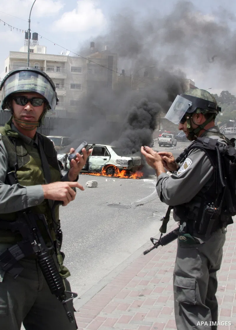 An Israeli border policeman rides past a car which was torched during riots in the East Jerusalem neighborhood of A-Tur, on 13 May 2011, as riots broke out in several flashpoints in East Jerusalem following the Friday Pr...