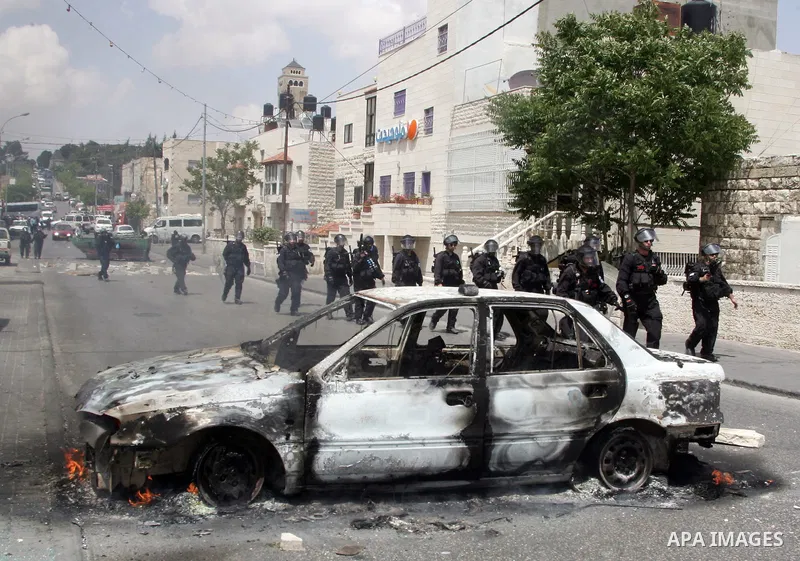 An Israeli border policeman rides past a car which was torched during riots in the East Jerusalem neighborhood of A-Tur, on 13 May 2011, as riots broke out in several flashpoints in East Jerusalem following the Friday Pr...