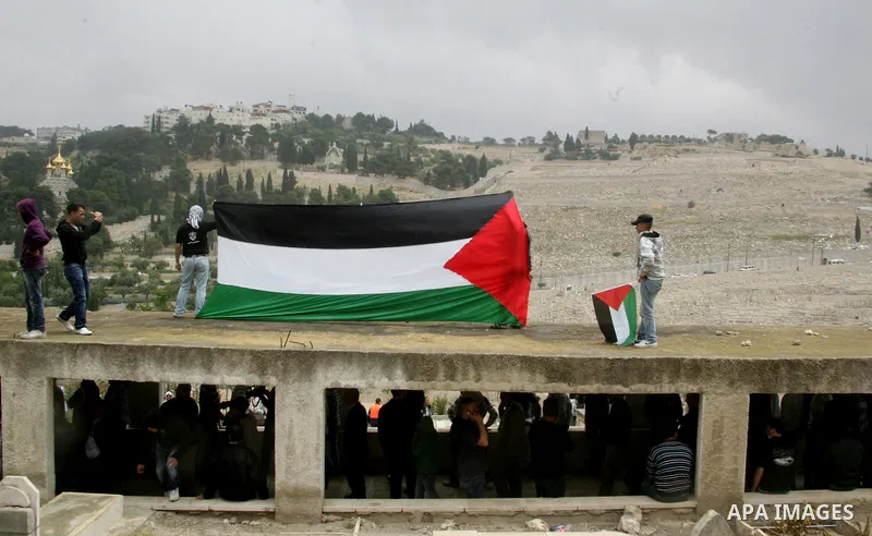 Palestinians hold national flag during clashes following the funeral of a teenager who died after being shot as Palestinians launched events to mourn the 1948 creation of the Jewish state in Jerusalem the day before, aft...