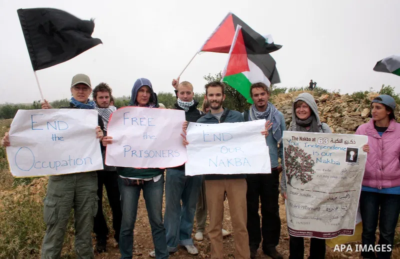 Protesters carrying flags demonstrate in front of Iraeli soldiers during the weekly demonstration in the West Bank village of Beit Omar , near Hebron against Israel's controversial separation barrier and to mark the 63th...