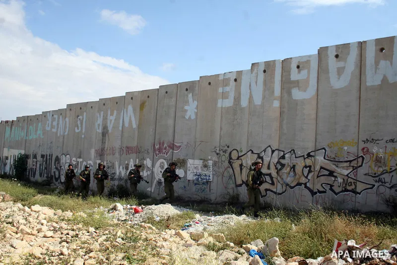 Israeli soldier walk past murals painted on the controversial Israeli separation barrier during clashes with Palestinian stone throwers at the Israeli manned Qalandia checkpoint between Jerusalem and the West Bank city i...
