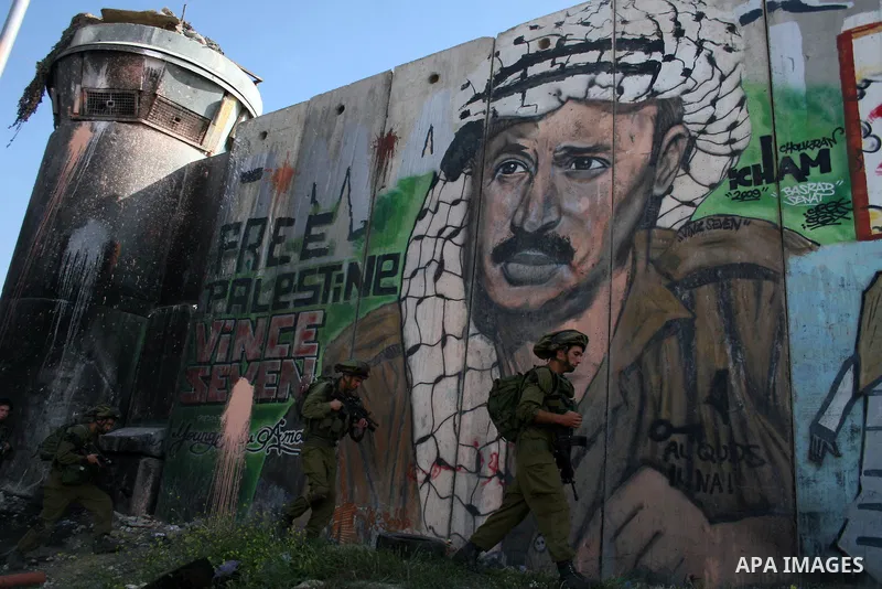 Israeli soldier walk past murals painted on the controversial Israeli separation barrier during clashes with Palestinian stone throwers at the Israeli manned Qalandia checkpoint between Jerusalem and the West Bank city i...