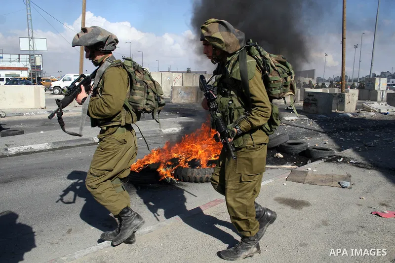 Israeli soldiers run past burning tires during clashes with Palestinian stone throwers at the Israeli manned Qalandia checkpoint between Jerusalem and the West Bank city if Ramallah on May 14, 2011, as Palestinians gathe...