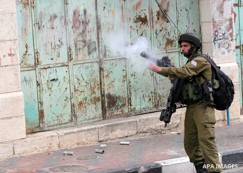 An Israeli soldier fires tear gas canister toward Palestinian youths during confrontations in the restive West Bank city of Hebron as heavy clashes broke out near Ramallah and Jerusalem while Palestinians mourned on May...