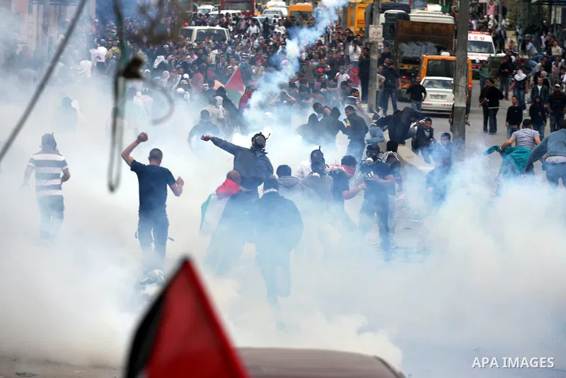 Palestinians run for cover as Israeli soldiers fire tear gas canisters during clashes with Palestinian stone throwers at the Israeli manned Qalandia checkpoint between Jerusalem and the West Bank city of Ramallah on May...