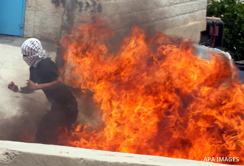 A Palestinian moves a burning tire as Israeli soldiers clashed with Palestinian stone throwers at the Israeli manned Qalandia checkpoin between Jerusalem and the West Bank city of Ramallah on May 15, 2011. Palestinians a...