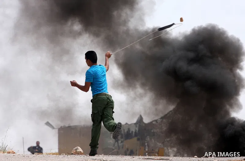 A Palestinian demonstrator uses a sling-shot to hurl stones at Israeli troops, not pictured, during the weekly demonstration against Israel's separation barrier in the West Bank village of Bilin, near Ramallah, Friday, M...