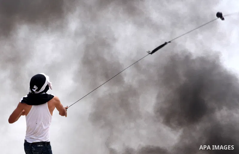 A masked Palestinian demonstrator uses a sling-shot to hurl stones at Israeli troops, not pictured, during the weekly demonstration against Israel's separation barrier in the West Bank village of Bilin, near Ramallah, Fr...