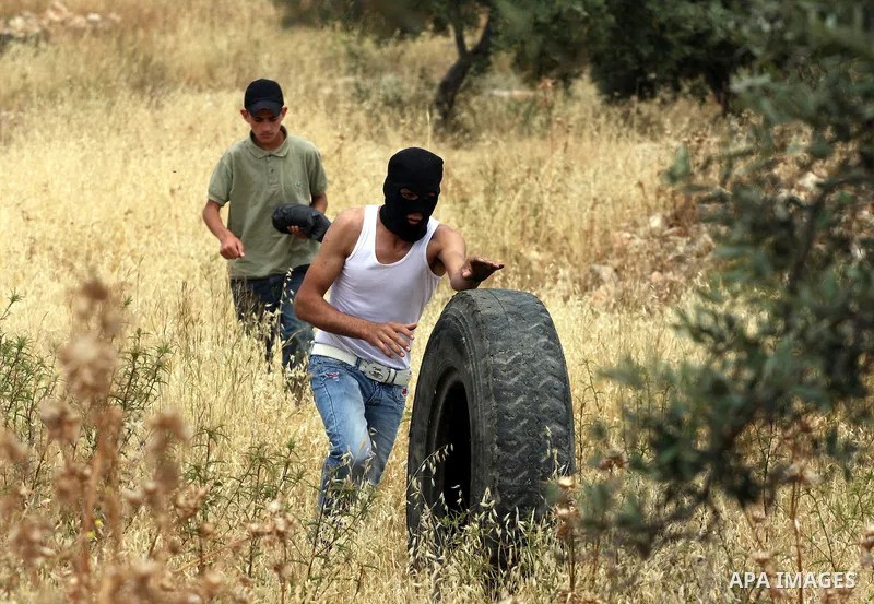 A masked Palestinian demonstrator prepares a tyre to be set ablaze during the weekly demonstration against Israel's separation barrier in the West Bank village of Bilin, near Ramallah, Friday, May 20, 2011. President Bar...