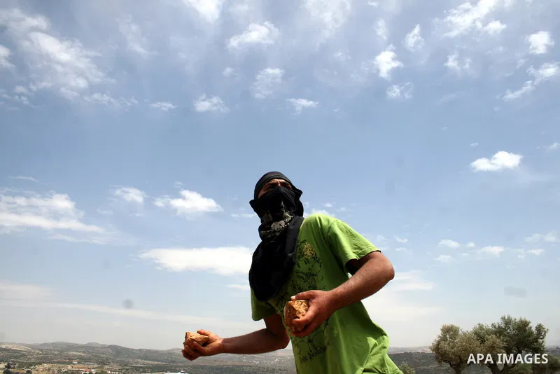 A masked Palestinian demonstrator hurls stones at Israeli troops, not pictured, during the weekly demonstration against Israel's separation barrier in the West Bank village of Bilin, near Ramallah, Friday, May 20, 2011....