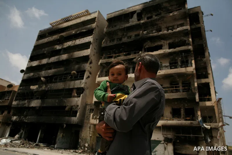 A man holding a baby stand in front of a building destroyed during clashes between rebel forces and Libyan Army loyal to leader Muammar Gaddafi in Misrata, Libya, May 26, 2011 Photo by Wissam Nassar