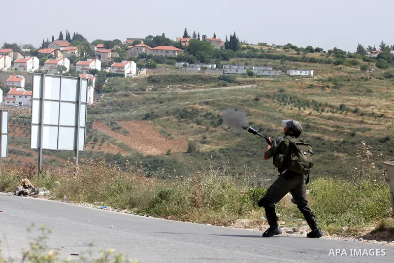 Israeli soldiers fire tear gas to disperse a protest against the expropriation of Palestinian land to expand the Jewish settlement of Halmish (background), in the West Bank village of Nabi Saleh, on May 27, 2011. Photo b...