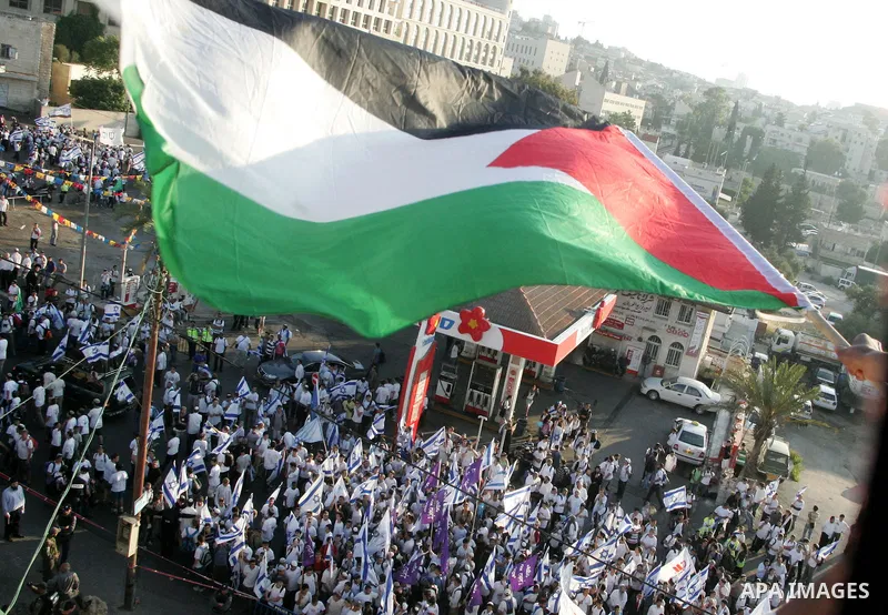 A Palestinian youth waves his national flag as Israelis march at Damascus Gate, the main entrance to the old city of Jerusalem, after they started chanting "Death to Arabs" while throwing vegetables, sticks and stones at...