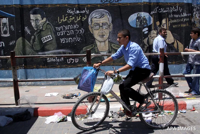 A Palestinian boy rides a bicycle in front of a mural depicting captured Israeli soldier Gilad Shalit in Gaza City on June 1, 2011. in the release of the captured soldier Versus for a thousand Palestinian prisoners . Sai...