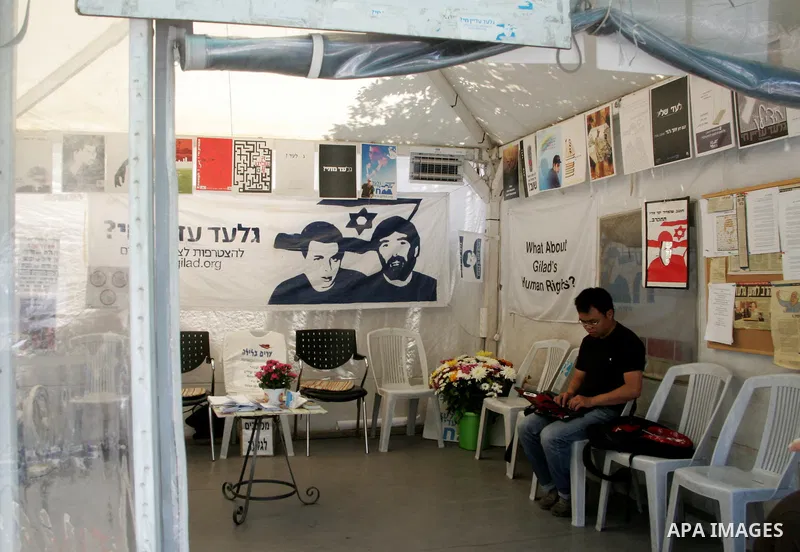 An Israeli activist sits next to a poster of abducted Israeli soldier Gilad Shalit, in the family's protest tent, outside Prime Minister Benjamin Netanyahu's residency in Jerusalem on June 2, 2011. Netanyahu's office den...