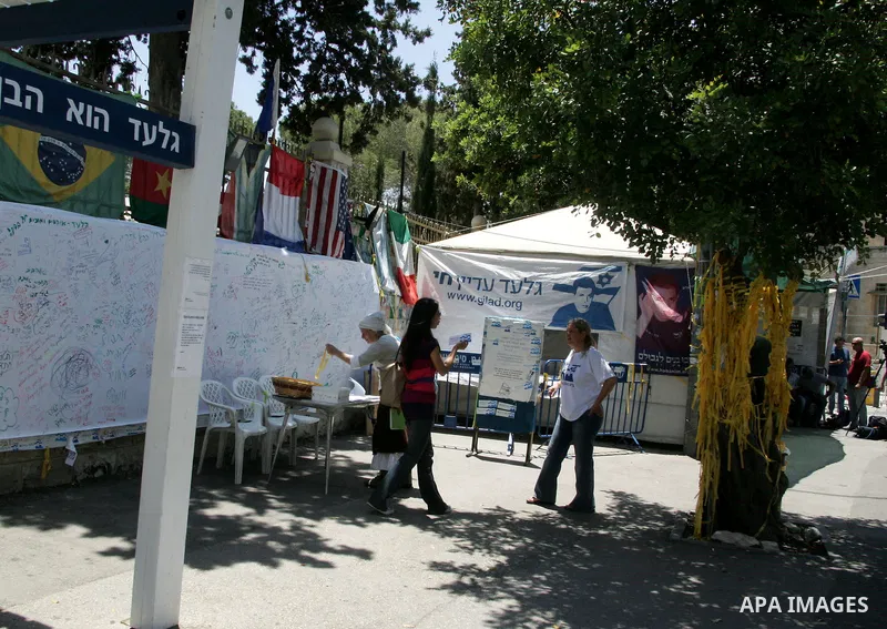 Israeli activists stand next to a poster of abducted Israeli soldier Gilad Shalit, in the family's protest tent, outside Prime Minister Benjamin Netanyahu's residency in Jerusalem on June 2, 2011. Netanyahu's office deni...
